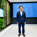 A visionary Vietnamese business leader in a modest, professionally tailored business suit, standing in a bright, modern sustainability innovation center in Ho Chi Minh City, with sleek, clean industrial design elements. In the background, subtle visual cues of circular economy are visible, such as recycled material displays, interactive screens showing resource flow diagrams, and a lush indoor vertical garden. The overall atmosphere is forward-thinking and committed to environmental stewardship. Perfect anatomy, correct proportions, natural pose, well-formed hands, proper finger count, natural body proportions, professional studio lighting, high resolution, soft ambient light, safe for work, appropriate content, fully clothed, professional dress, family-friendly.